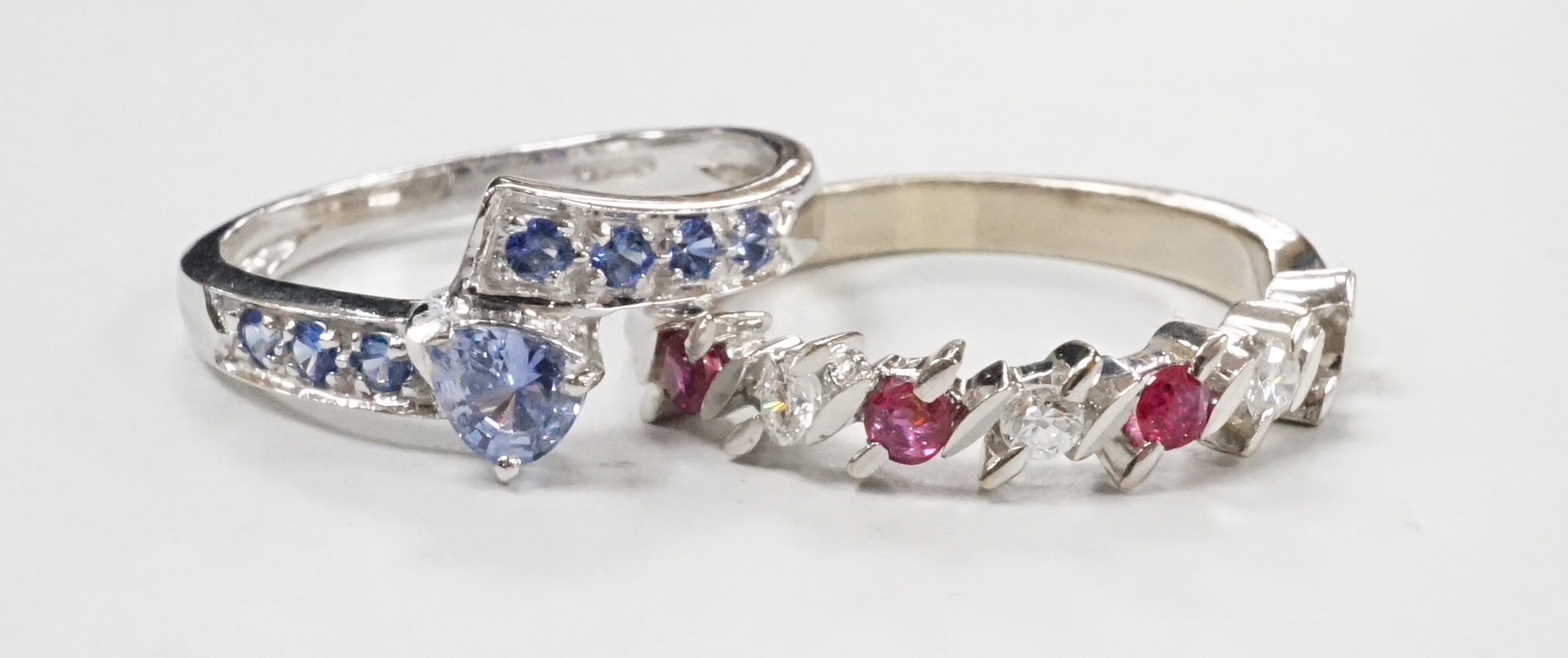A modern continental white metal ruby and diamond set half hoop ring (ruby missing), size P and and a modern 18ct white gold and blue gem set crossover ring, size N/O, gross weight for both, 7.1 grams.
